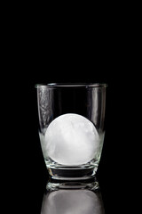 ice ball inside cocktail glass on a reflective black table.