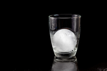 ice ball inside cocktail glass on a reflective black table.