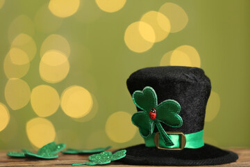 Leprechaun hat and clover leaves on wooden table against blurred lights, space for text. St...