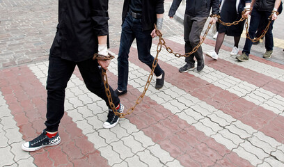 people with chain on hands of chained together are walking and cross over red lines of crosswalk on...