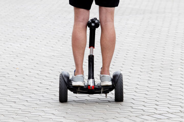 feet of a man riding on a two weels self-balancing scooter on sidewalk on a street in a city close up