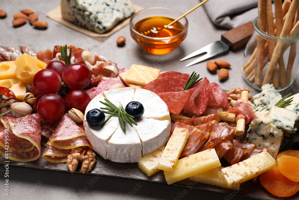 Wall mural Wooden board with different appetizers on grey table, closeup