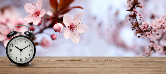 Black alarm clock on wooden table, space for text. Daylight saving time (Spring forward)