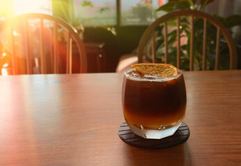 glass of cold black orange coffee on wooden table in cafe