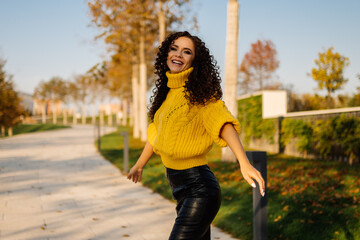 In a casual skirt and a warm yellow sweater of a large knitting on the park path comes a beautiful...