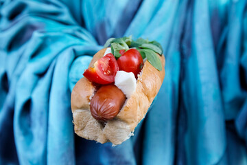 delicious hot dog with sausage, basil, mozzarella and tomatoes closeup in hand of painted like a statue woman, American fast food concept.