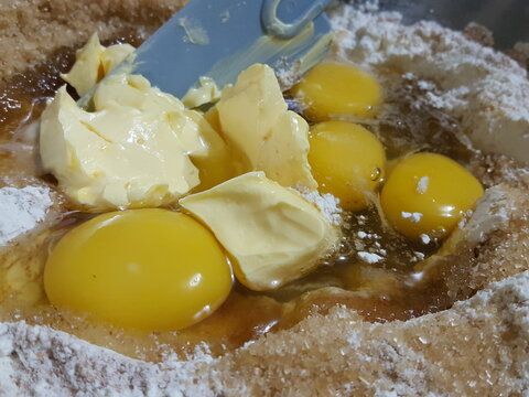 Close up of ingredients to make a cake. Eggs yokes, Butter Flour, and some sugar. A blue spatula is also in the shot. 