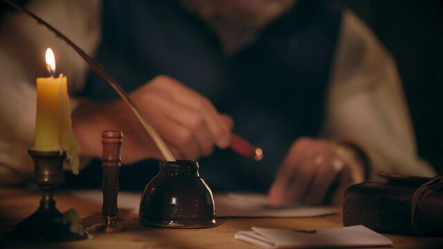 An 18th century scene of a man in a room lit by light from an overhead window and a candle who uses sealing wax stamp to secure the letter he has written before turning it over and address