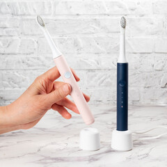 Electric toothbrushes charge on white background. Female hand holding electric toothbrush.