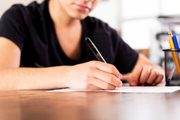 Close-up of the hand of a teenage student filling out an application at a desk at home. Concept of...