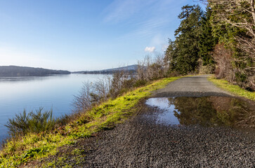 View of calm water, blue sky, and mountains from the Galloping Goose Trail in East Sooke, Vancouver Island