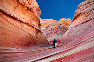 Man tourist hiking in Arizona canyon with textured red walls. The Wave, Paria Canyon. Kanab. Utah. United States of America  - obrazy, fototapety, plakaty
