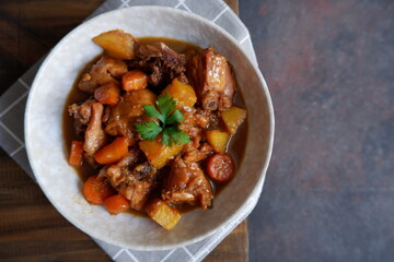 a plate of chicken stew with carrot and potato on a wooden table