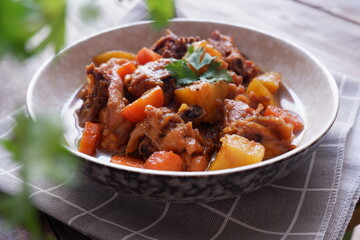 a plate of chicken stew with carrot and potato on a wooden table