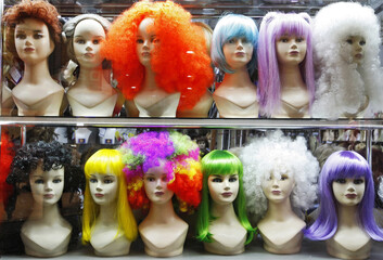 lots of multicolored female wigs on mannequin heads in a shop window 