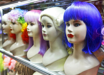 lots of multicolored female wigs on mannequin heads in a shop window 