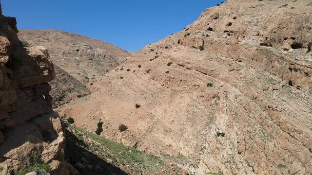 Aerial Drone shot of dry valley and mountains at Binyamin Region in Blue sky, Judea and Samaria Area, Israel. Israeli desert canyon with vegetation. Drone between mountains 4K