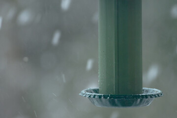 Green metal bird feeder with snow lightly falling landscape