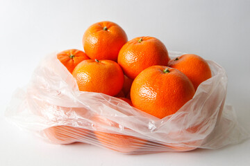 mandarins, tangerine citrus fruits in plastic bag on white background, shadow to the right