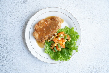 a plate of crispy chicken steak and vegetables with black pepper sauce in white background 
