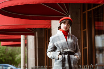 young european woman in gray coat and red scarf outdoors on a spring sunny day