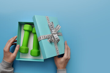 Green dumbbells in a gift box in the hands of a person. Sports and a healthy lifestyle in the modern world