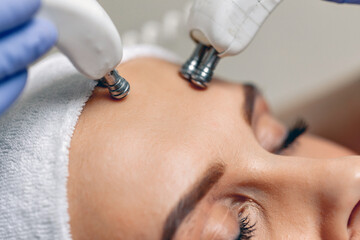 Close-up of microcurrent therapy procedure over the face of a young attractive girl in a beauty parlor. Reception with a beautician. Female beauty concept