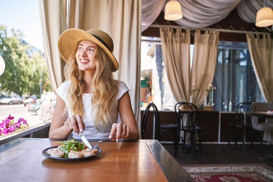 Young Woman At Restaurant Eating Shrimp Salad. Health Food Concept. Fork And Knife. Ountdoor Cafe. Hands Near Plate. Mediterranean Diet Meal. Female Person In Hat