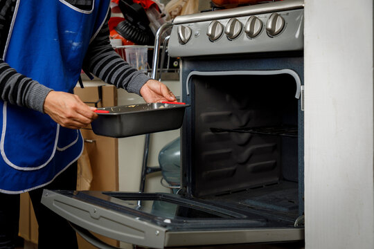Reposter&iacute;a en casa. Mujer metiendo un panque al horno de la estufa para cocinarlo.
