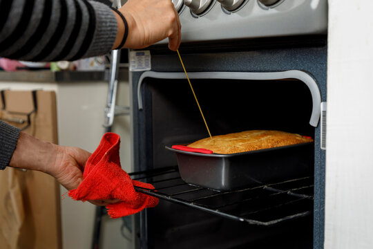 Reposter&iacute;a en casa. Mujer revisando la cocci&oacute;n de un panque en el horno de la estufa.