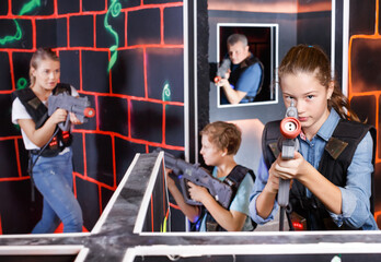 Fototapeta na wymiar Emotional teen girl with laser pistol playing laser tag with family at dark labyrinth