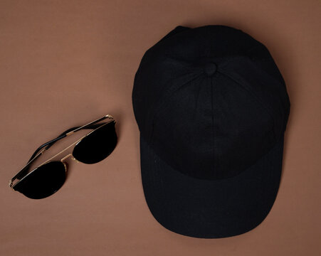 Blank baseball caps are used for design mockups. The hat on the side of an old camera and sunglasses. Plain hat isolated on brown background. Take a picture of a hat ready to be displayed. Mockup hat.