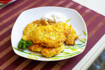 Appetizing zucchini pancakes with herbs on a white plate on the table.