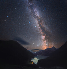 Photograph of the night sky. Milky Way over a mountain lake. There are many small stars throughout...