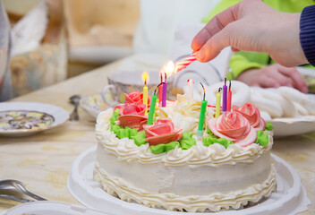 A hand lights candles on a birthday cake.