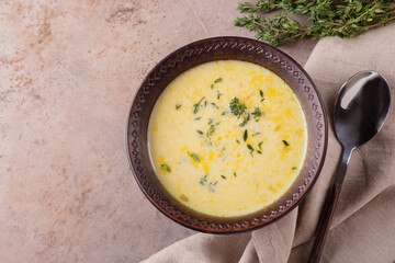 A bowl of cheese soup with thyme and spoon on a beige background with copy space. Vegetarian food. Top view.