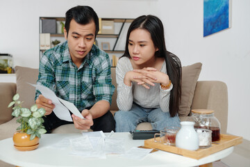 Vietnamese young man showing bills to girlfriend when they are discussing and managing personal expenses and utility bills