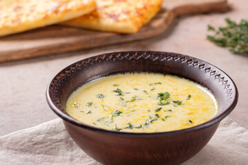 A bowl of cheese soup with thyme and bread on a beige background. Vegetarian food.