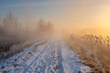 Fototapeta na wymiar The road leading dike between the lakes during the frosty, foggy sunrise