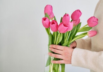Woman putting flowers in vase. Composing bouquet. Bouquet pink tulips in glass vase. Woman holding tulips in her hands, florist, floristry. Place for text