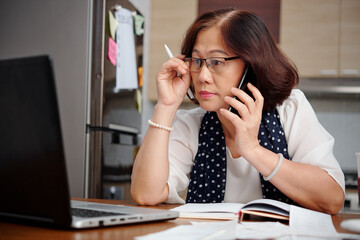 Elderly businesswoman working from home, she is taking on glasses when reading article on laptop...