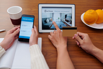 Hands of young couple checking banking account via mobile app when choosing apartment to rent or buy on tablet computer
