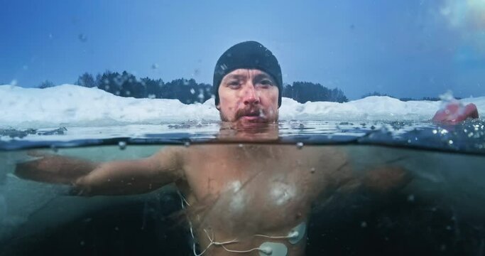 Medical test in the cold. Young man swims in the icy water with medical electrodes connected to his body and looks at the camera