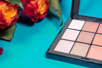 decorative composition with cosmetics and flowers. red roses and palette of pastel eyeshadow on blue background