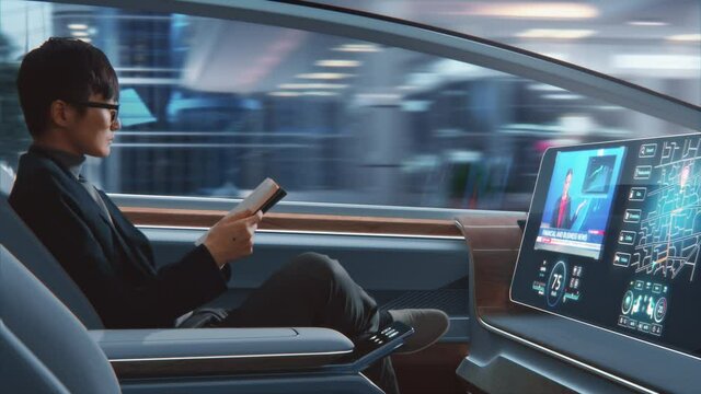 Futuristic Concept: Handsome Stylish Japanese Businessman in Glasses Reading Notebook and Watching News on Augmented Reality Screen while Sitting in a Autonomous Self-Driving Zero-Emissions Car. 