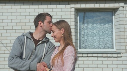 Fototapeta premium A loving husband kisses his wife in front of his house.