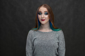 Portrait of caucasian young beautiful brunette woman with dyed hair and bright makeup smiling on a blurred gray background, close up