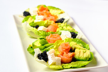 Lettuce boats with salmon, goat cheese, avocado and caviar, healthy and gourmet food to make a starter, photographed on a completely white background