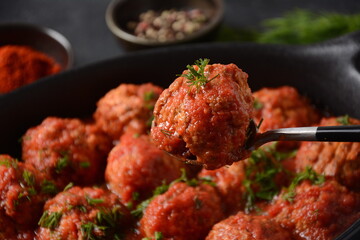 Boulettes de Poisson, Fried Fish Balls in Tomato Sauce in a black dish on a concrete table with ingredients