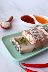  Uncooked boneless pieces of threadfin fish. Raw Dadha fish cubes placed on a blue plate. clean fish fillets with skin on. Recipe ingredients such as rock salt, coriander, and spices. Copy space.